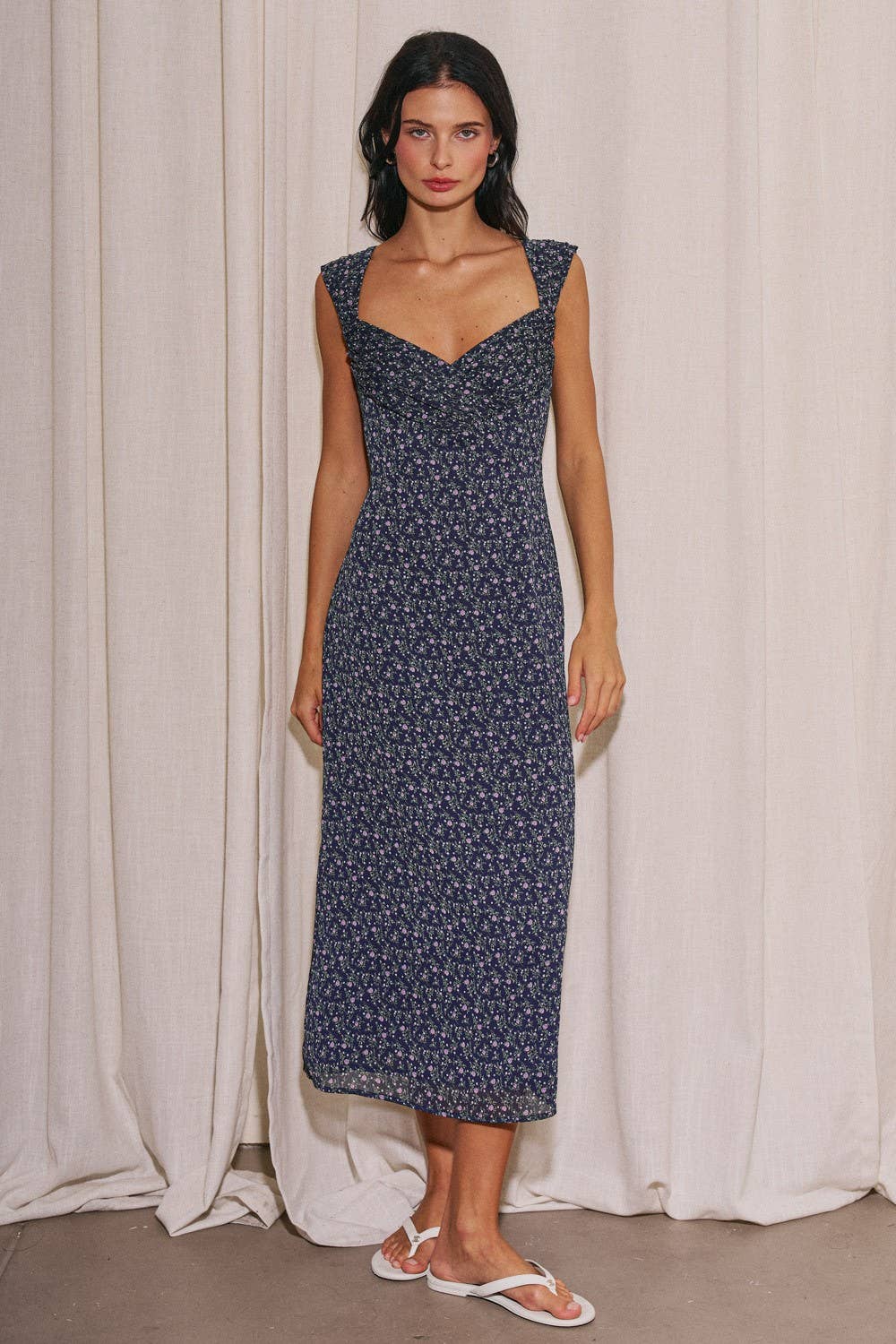 Woman wearing a navy floral dress against a white curtain background