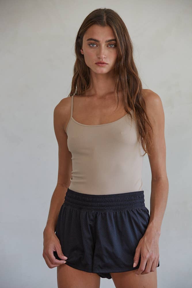 Woman wearing a beige tank top and black shorts against a plain background