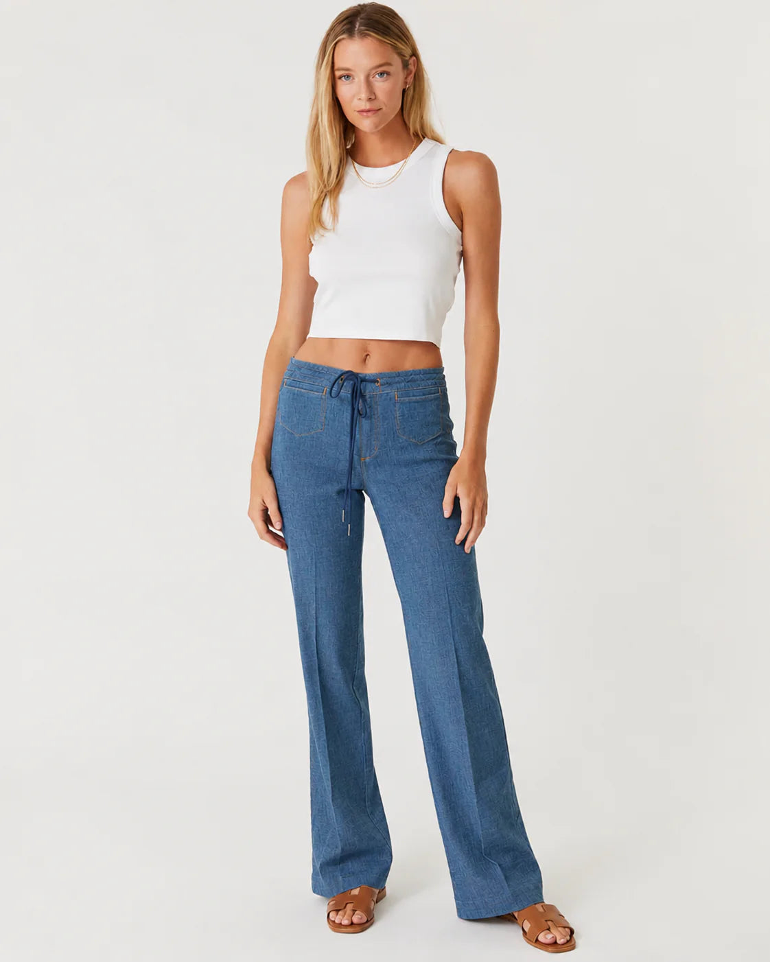 Woman in a white tank top and blue trousers on a white background.