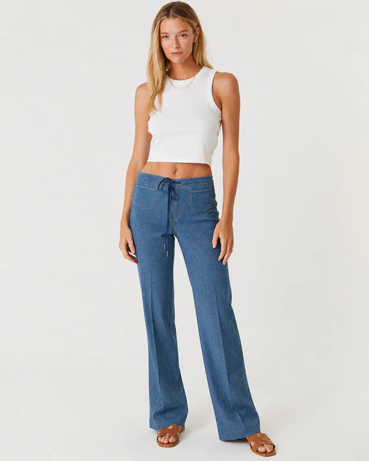 Woman in a white tank top and blue trousers on a white background.