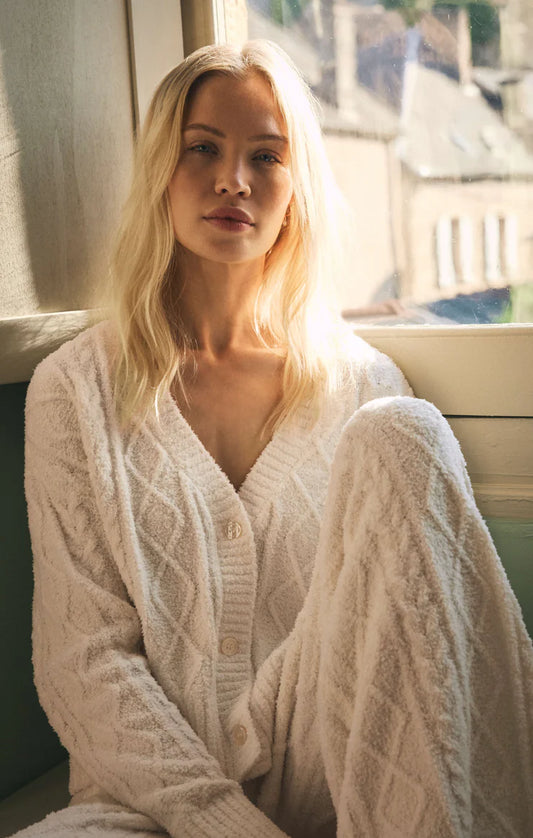 Woman wearing a white cable knit robe sitting by a window.