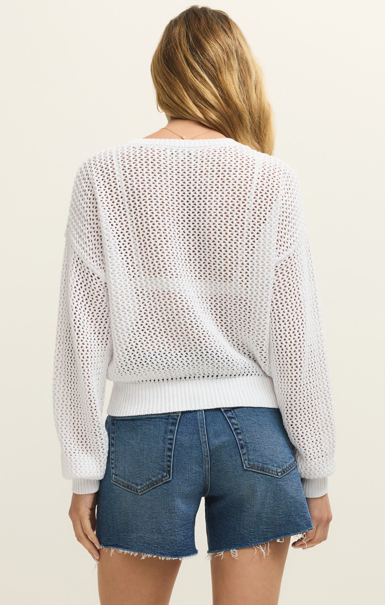 Person wearing a white mesh top and blue denim shorts on a plain background