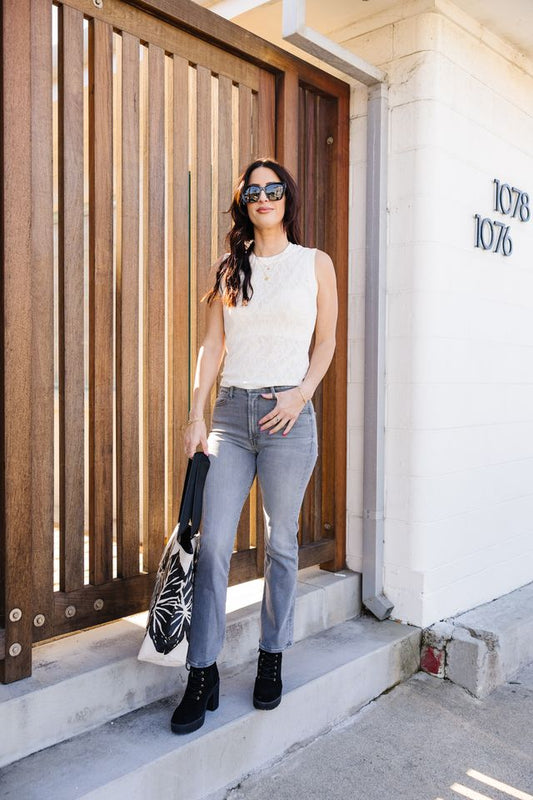Woman in white sleeveless top and blue jeans standing in front of a wooden door.