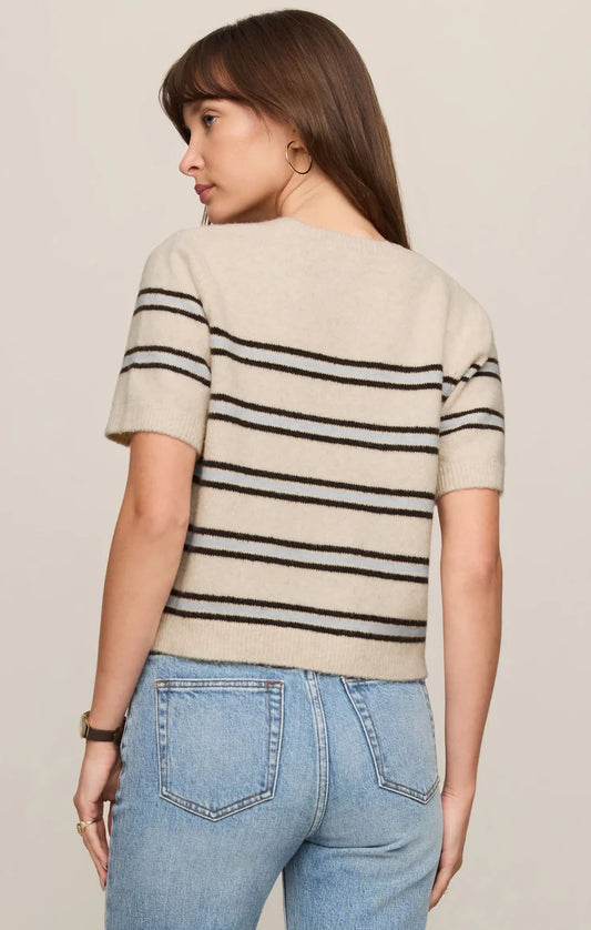 Woman wearing a beige sweater with black stripes and blue jeans on a plain background