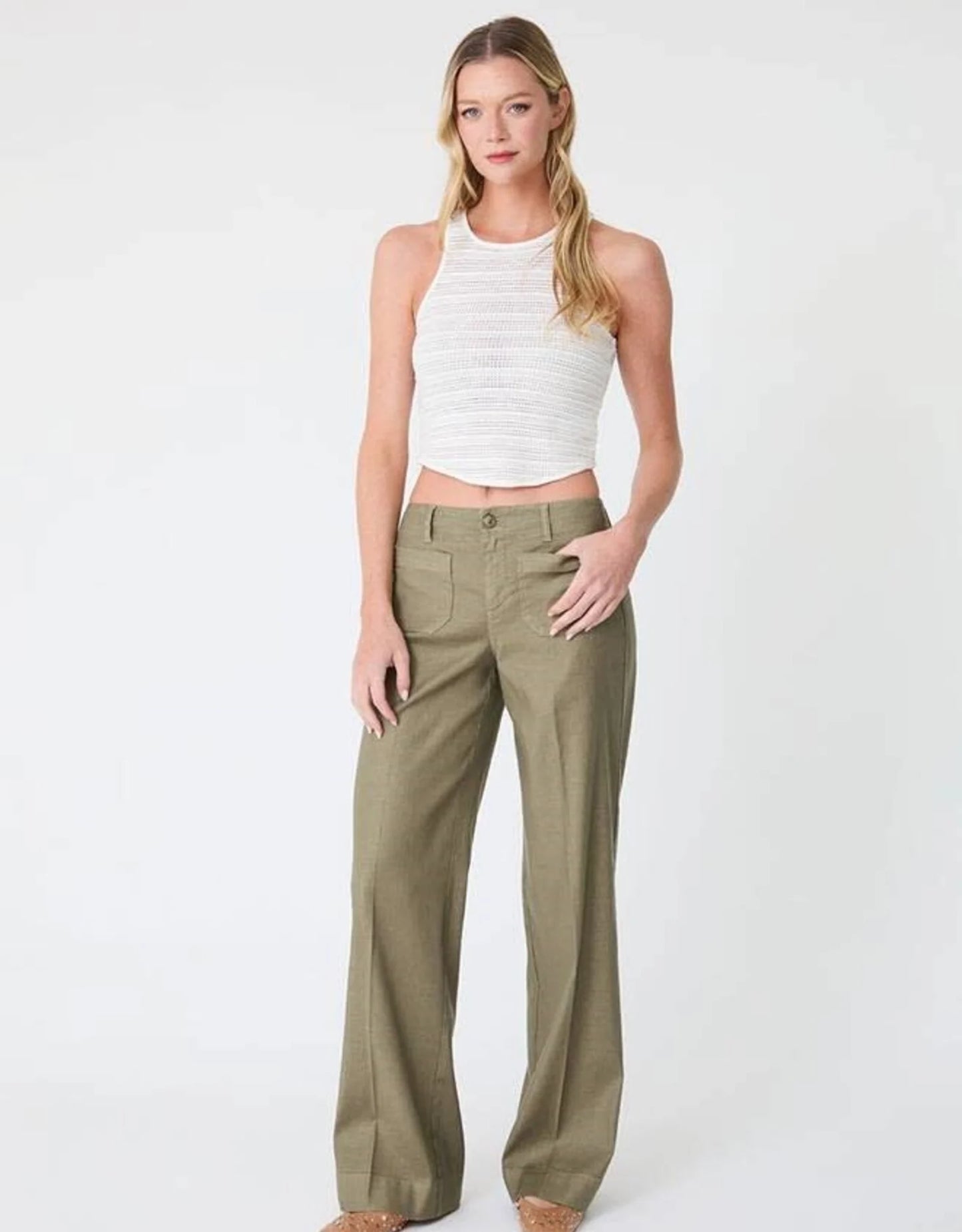 Woman in white crop top and green pants on white background.