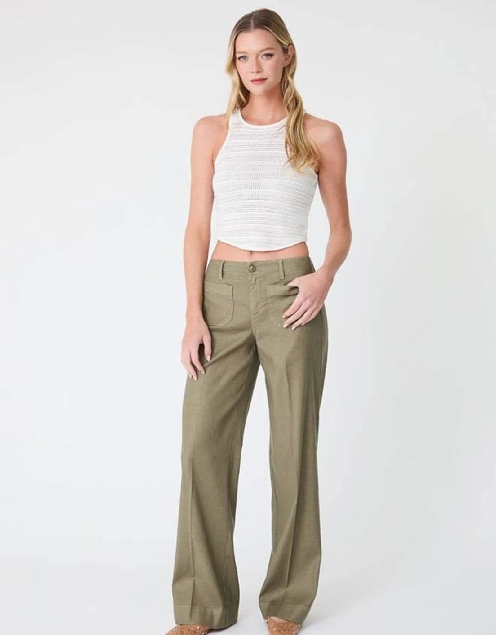 Woman in white crop top and green pants on white background.