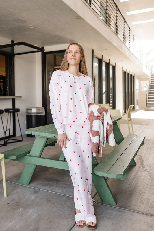 Woman in a white outfit with red patterns standing next to a green picnic table.