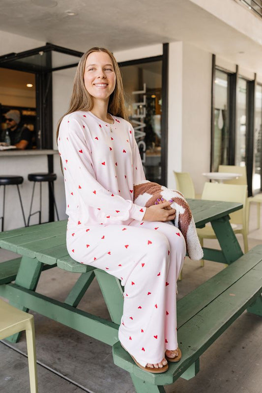Woman in a white outfit with red patterns sitting on a green picnic table in an indoor setting.