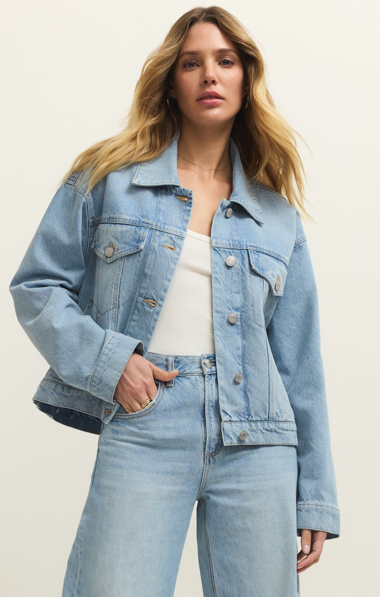 Woman wearing a light blue denim jacket and jeans on a plain background