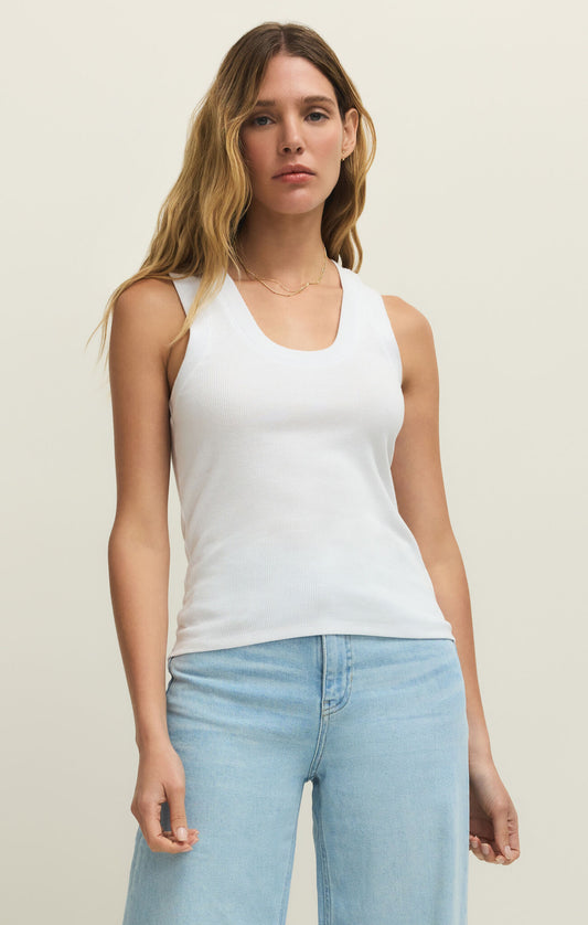 Woman wearing a white tank top and light blue jeans against a plain background