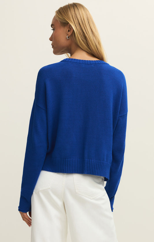 Person wearing a blue sweater and white pants on a plain background