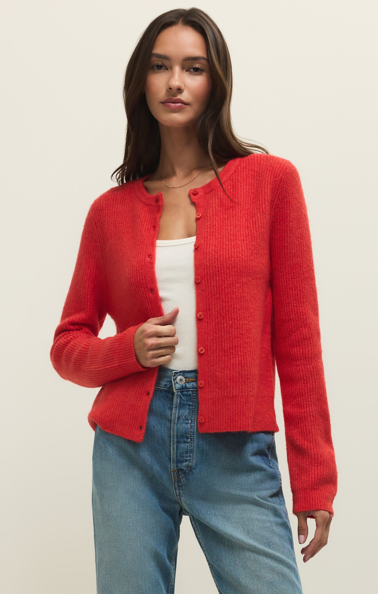 Woman wearing a red cardigan over a white top and blue jeans on a beige background
