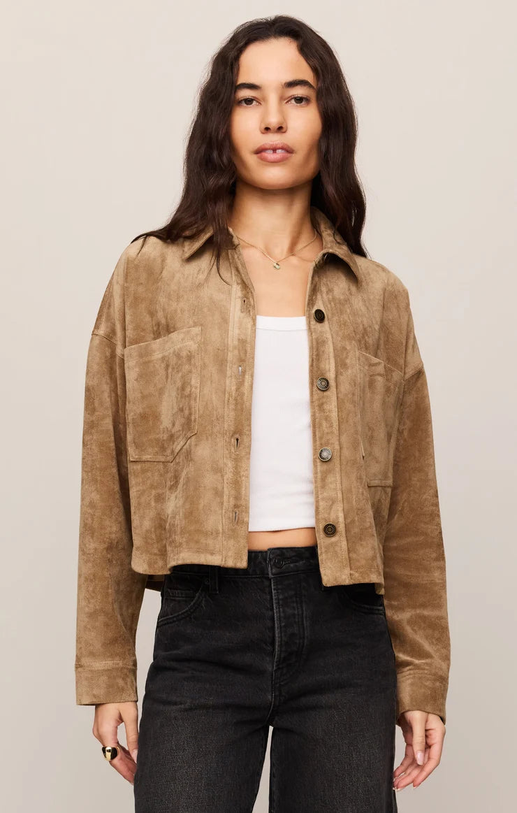 Woman in cropped brown jacket, white shirt, and black jeans on a white background.