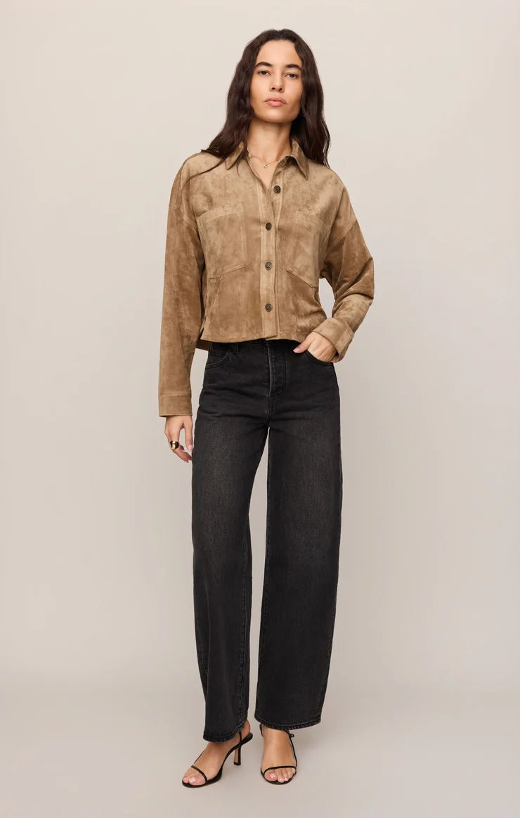 Woman in cropped brown jacket, white shirt, and black jeans on a white background.