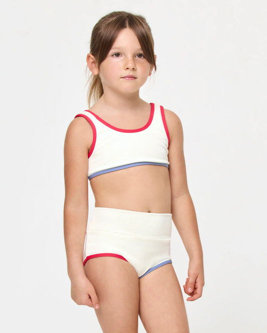 Young girl wearing a white bikini with red trim on a light gray background