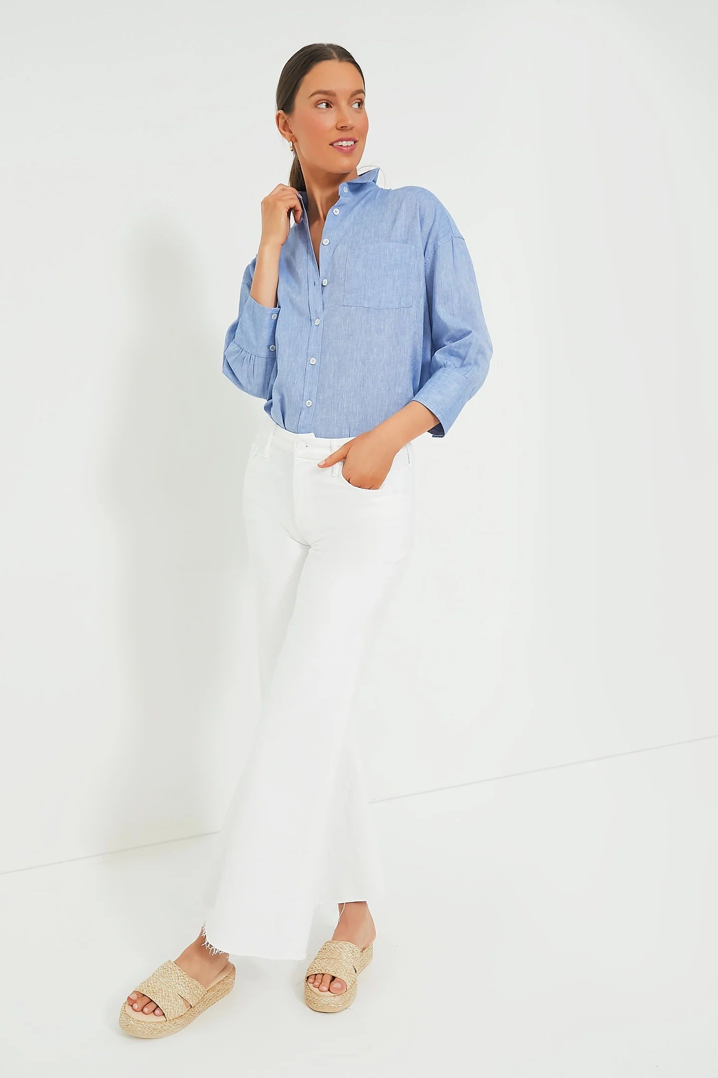 Woman wearing a blue button-up shirt and white pants on a white background