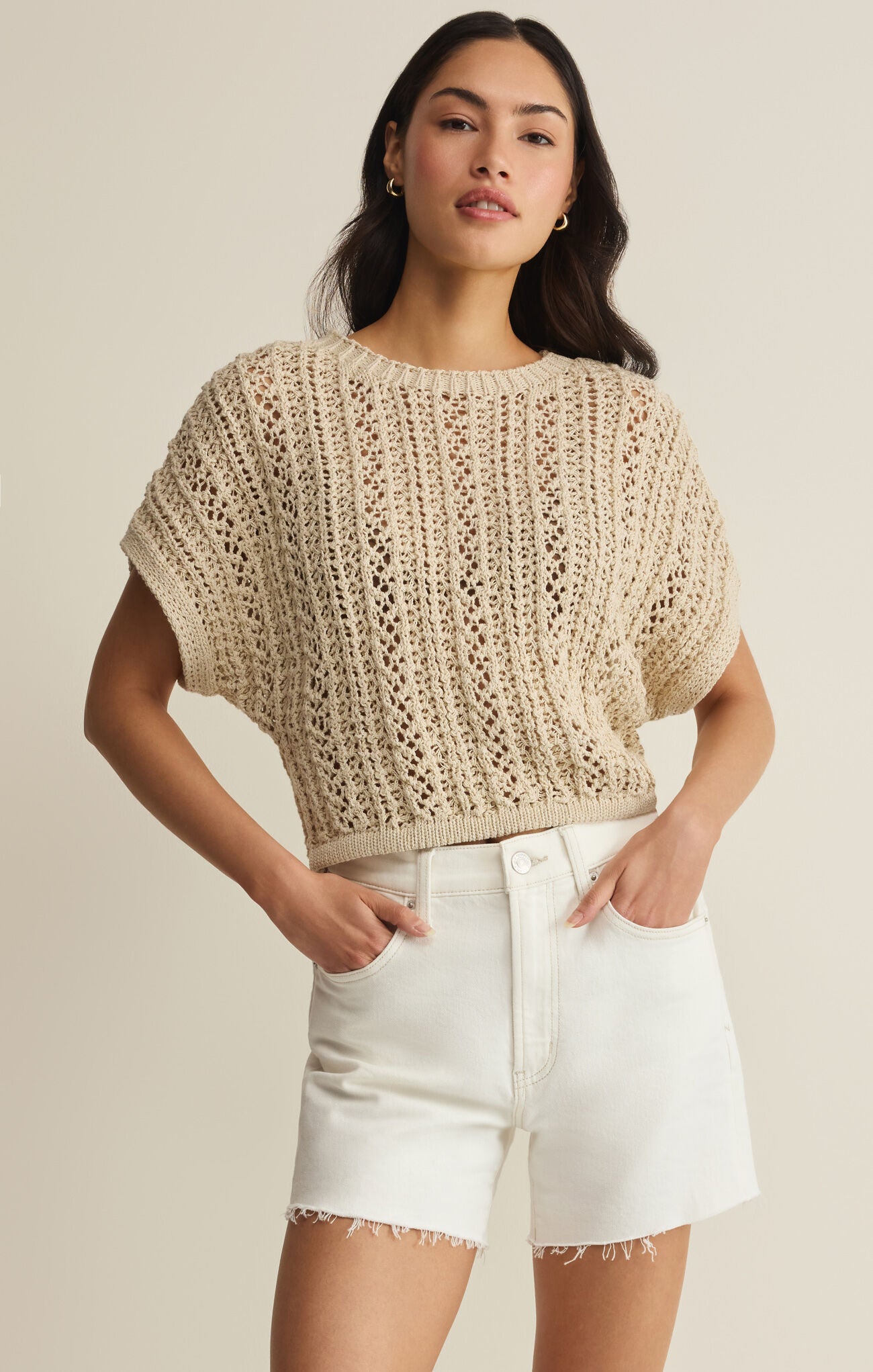 Woman wearing a beige crochet top and white shorts on a beige background
