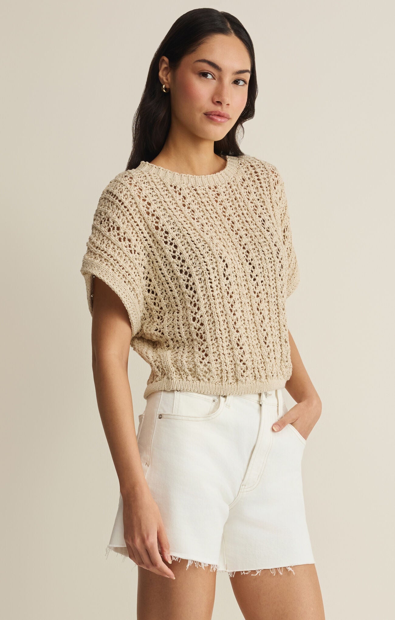 Woman wearing a beige knitted top and white shorts on a beige background