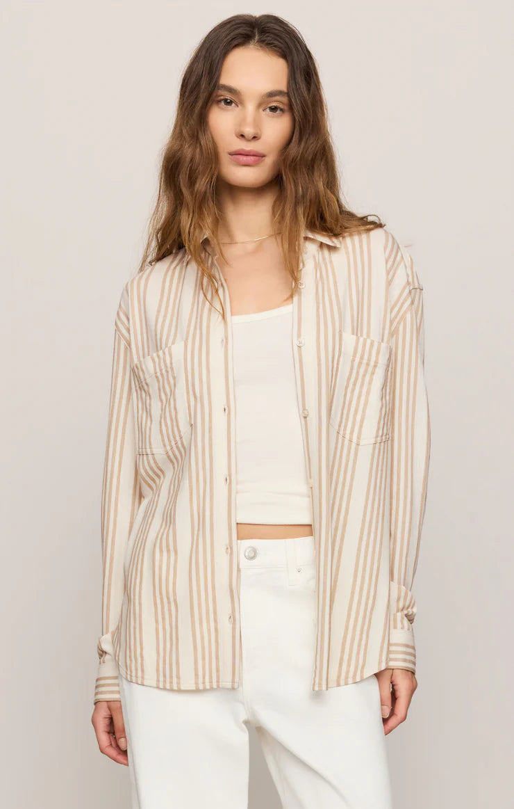 Woman wearing a striped shirt over a white top and pants on a plain background