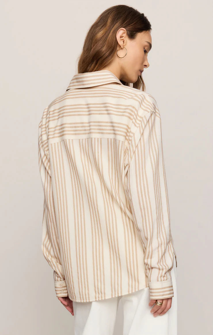 Woman wearing a beige and brown striped shirt against a plain background