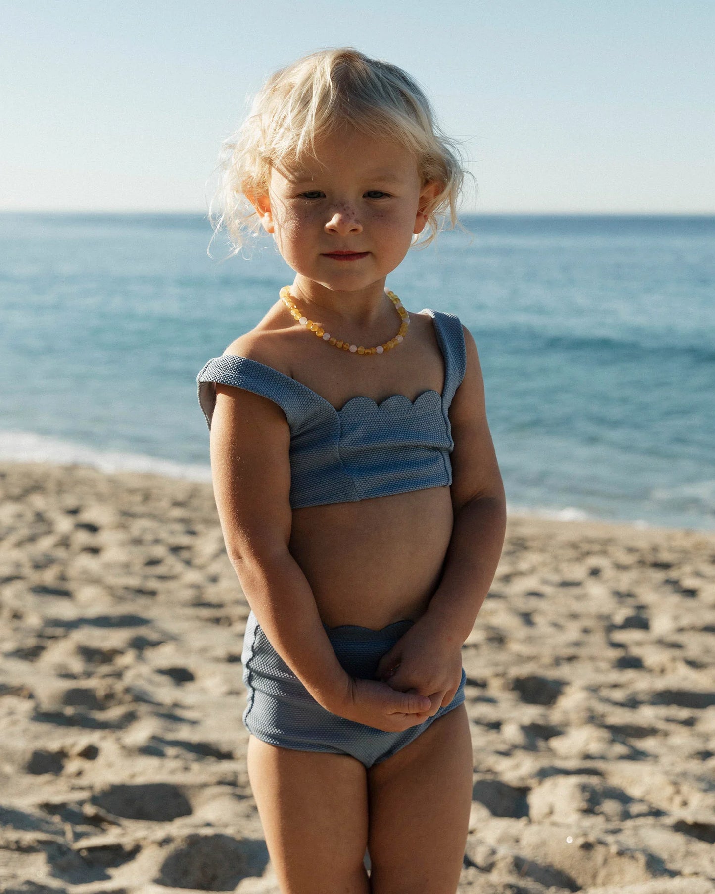 Young girl in a blue swimsuit standing on a beach with ocean in the background