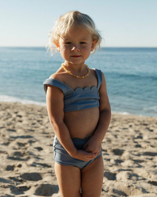 Young girl in a blue swimsuit standing on a beach with ocean in the background