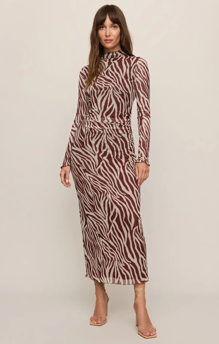 A woman modeling a long-sleeve mock-neck midi dress with a brown and beige zebra print, standing against a plain light beige studio background.