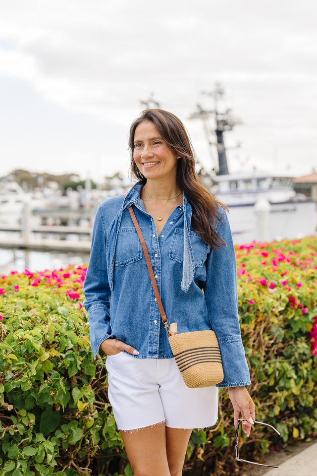 Woman wearing white shorts and blue denim top with a harbor background.