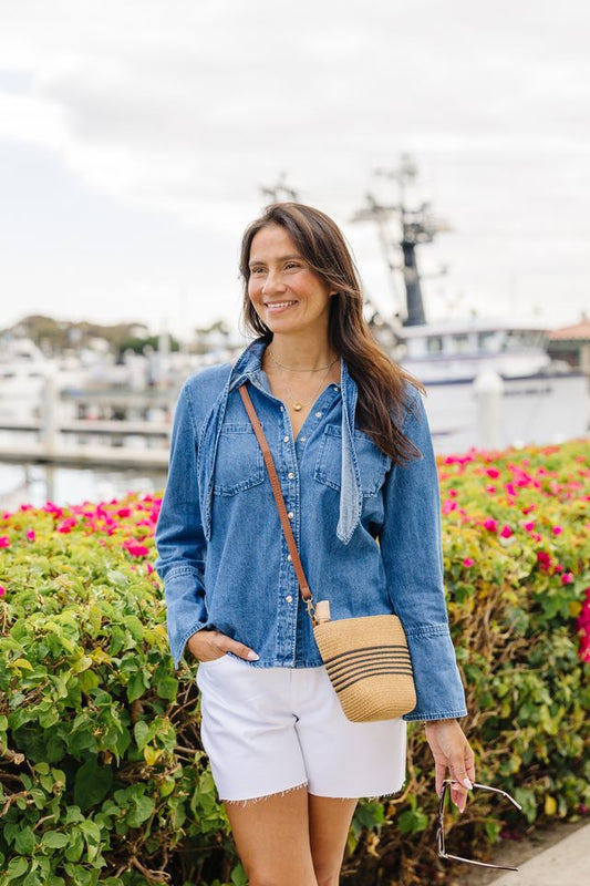 Woman wearing white shorts and blue denim top with a harbor background.