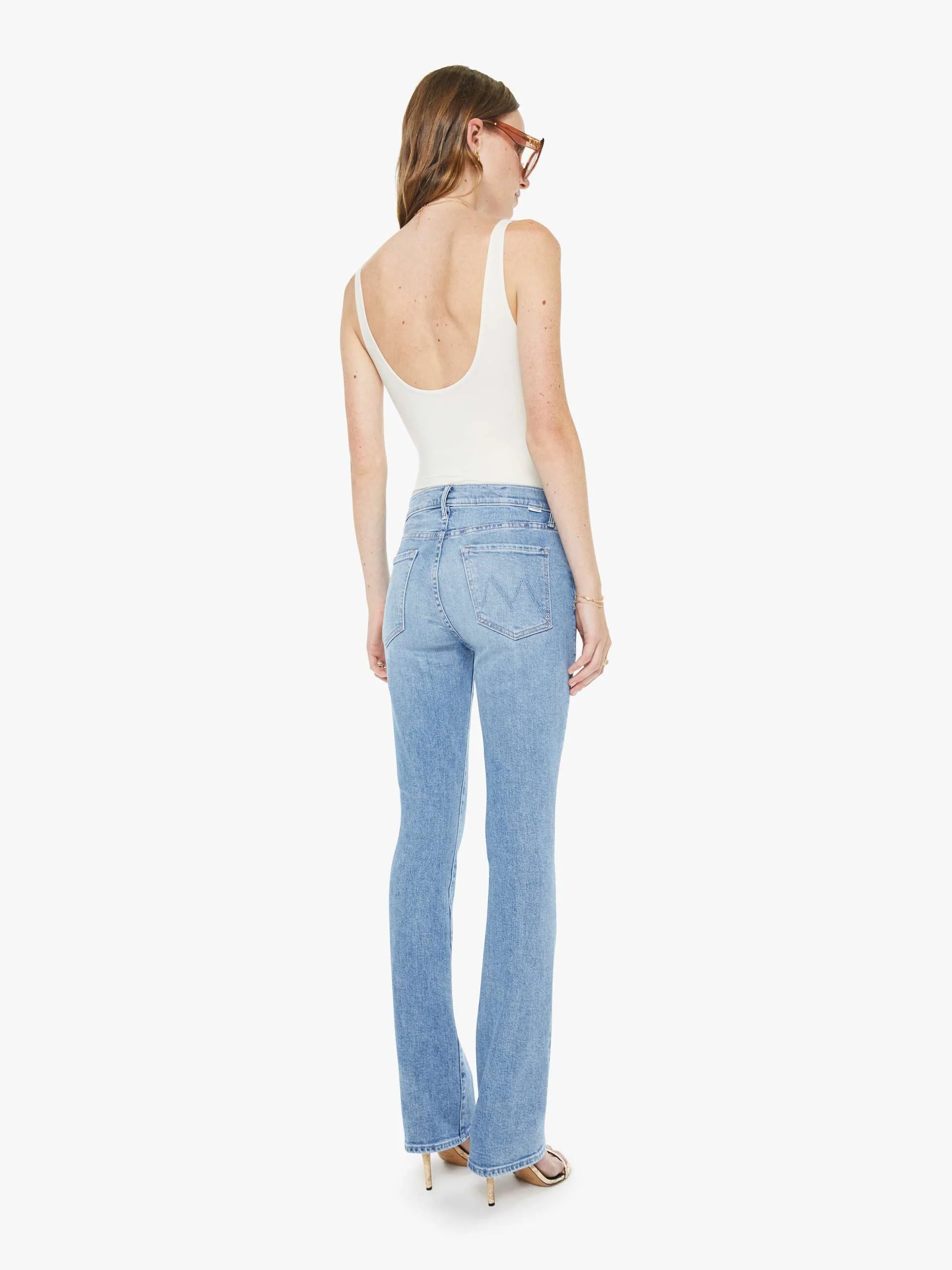 Woman wearing light blue jeans and a white top on a white background