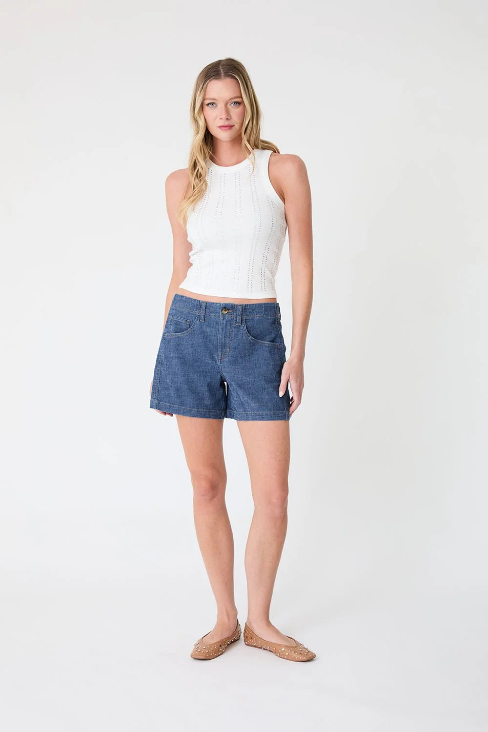 Woman wearing a white sleeveless top and blue denim shorts on a white background