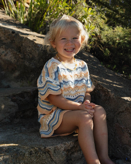 Young girl sitting on a rock outdoors wearing a patterned set.