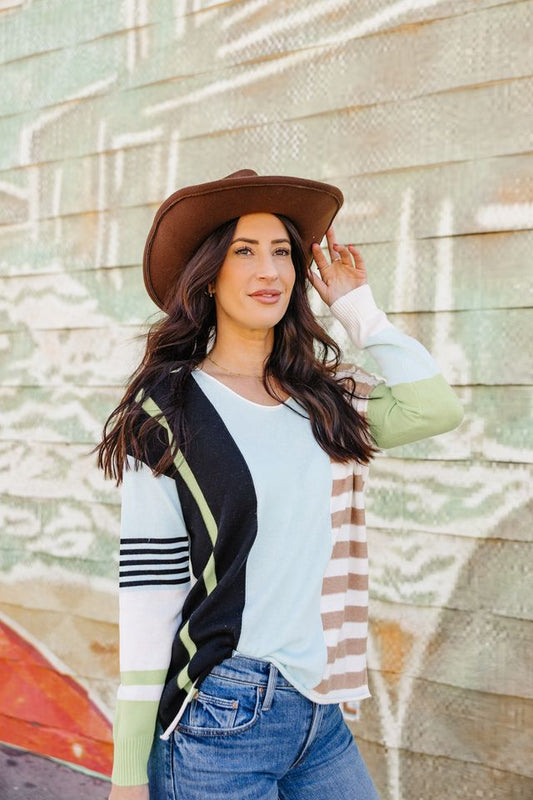 Woman wearing a brown hat, light blue shirt, and jeans against a textured wall.