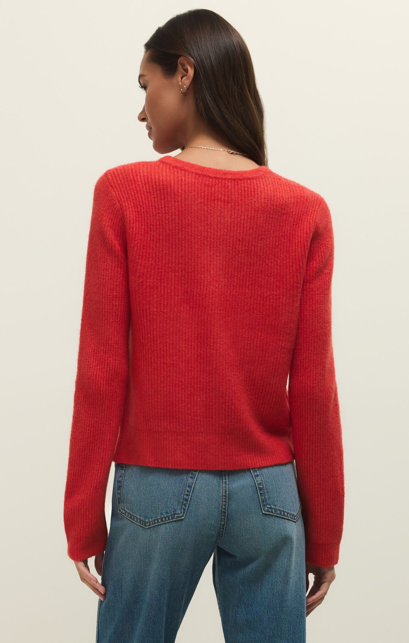 Person wearing a red sweater and blue jeans on a beige background