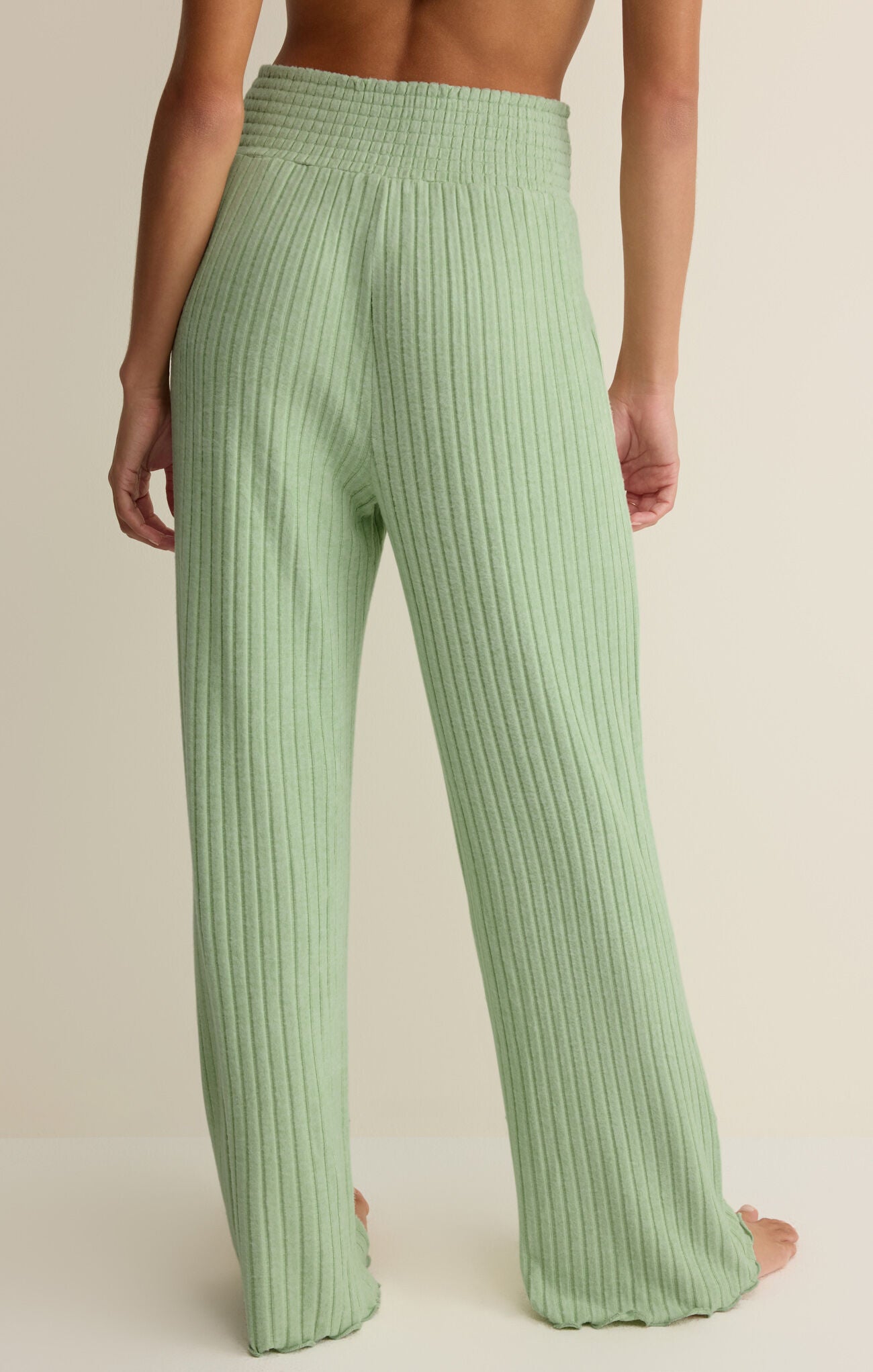 Green ribbed pants worn by a person on a beige background