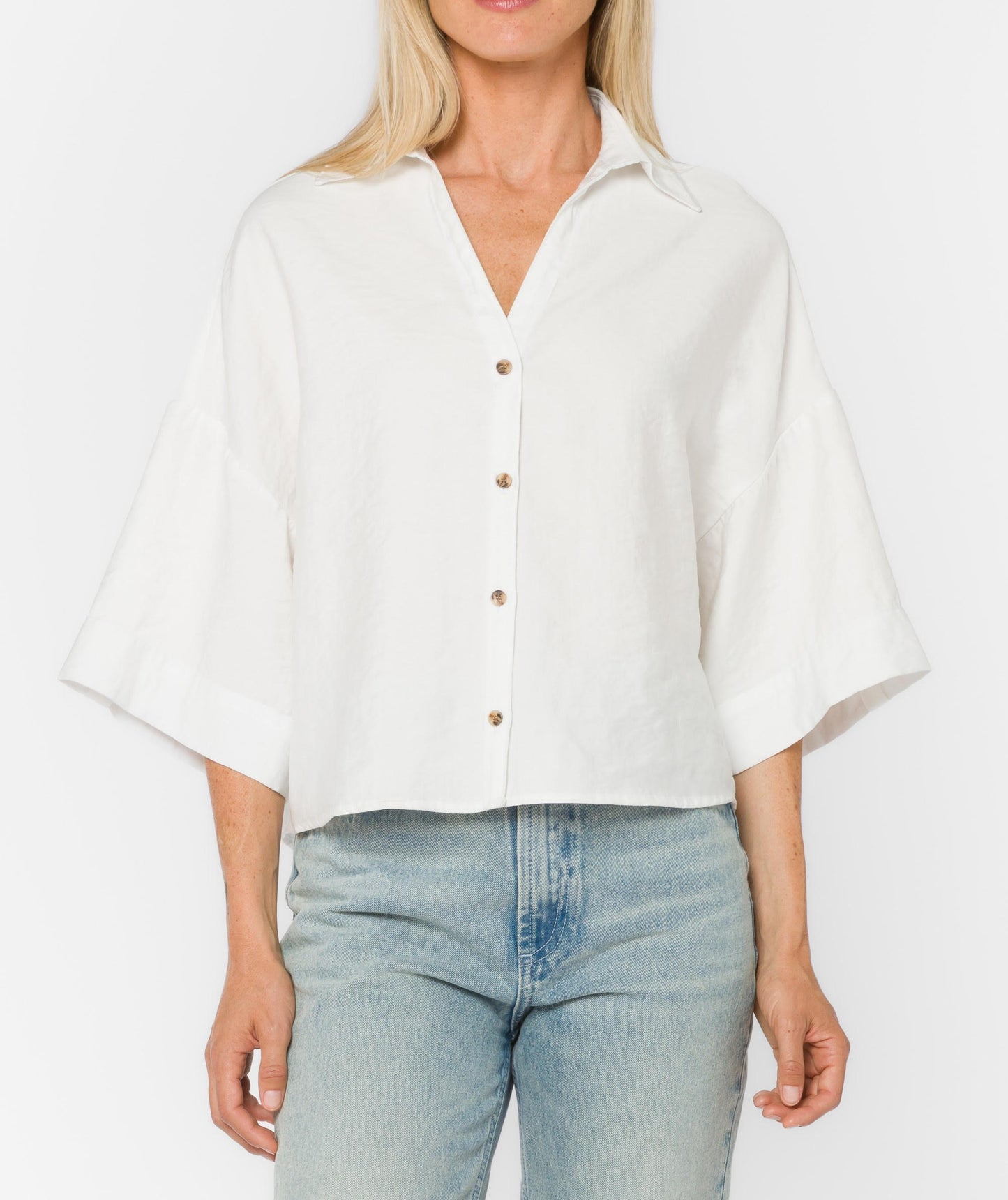 Woman wearing a white blouse with short sleeves and light blue jeans on a plain background