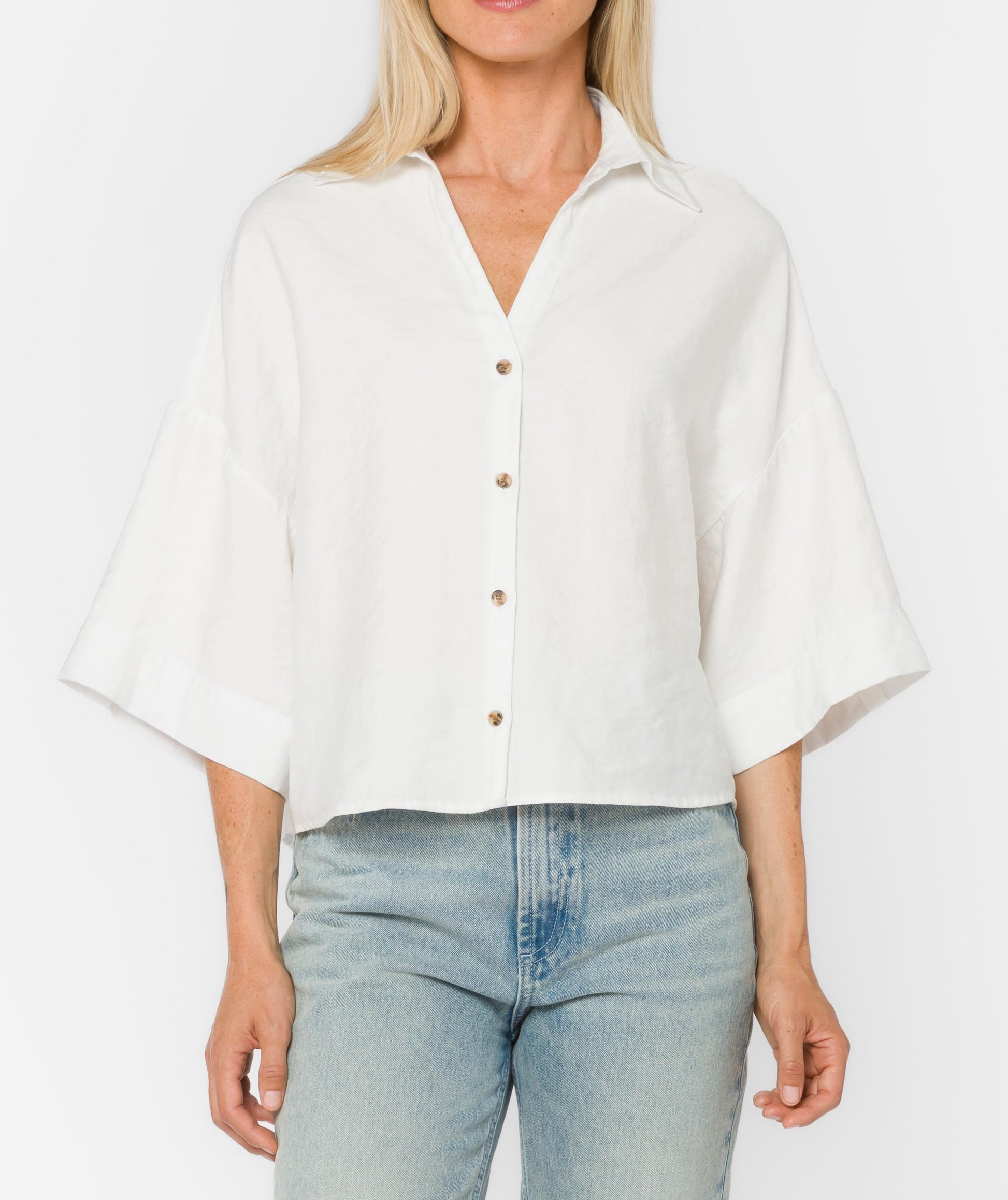 Woman wearing a white blouse with short sleeves and light blue jeans on a plain background