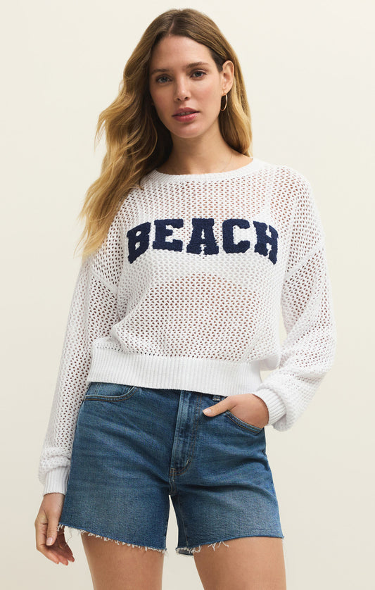 Woman wearing a white sweater with 'BEACH' text and denim shorts on a plain background